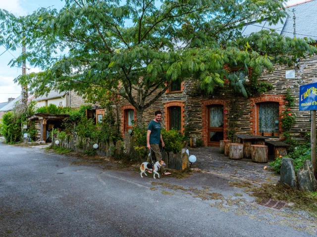 Promeneur et son chien passant devant un gîte en pierre avec terrasse arborée